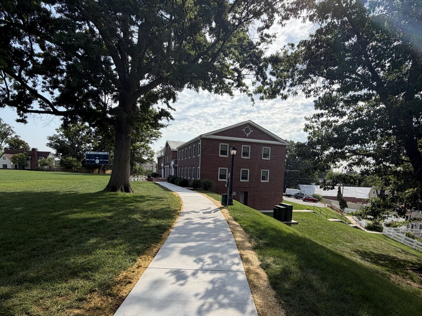 Maintained campus grounds — mown lawn, mature trees and a concrete walkway to the building
