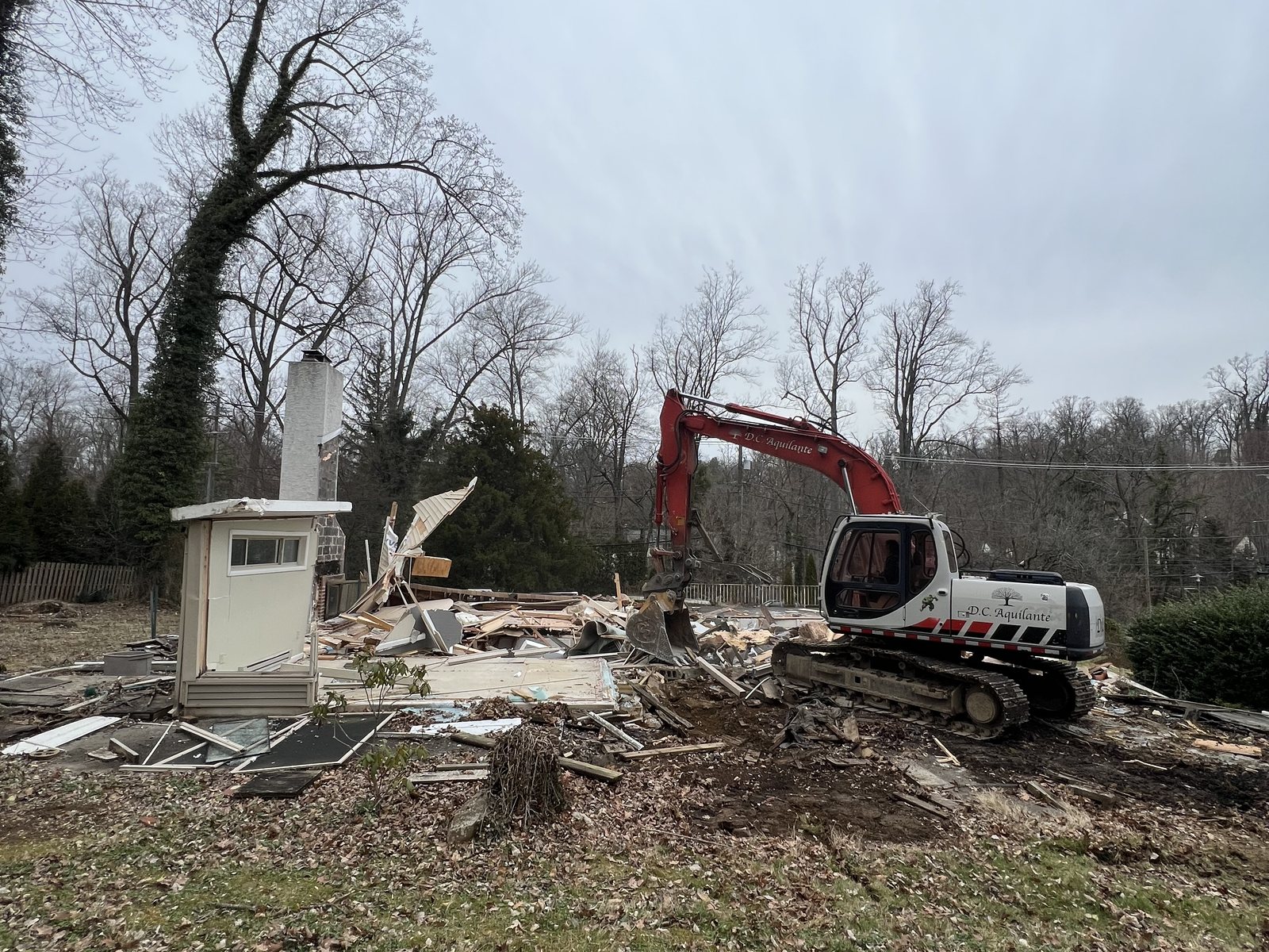 Excavator taking down a structure and loading debris during a residential demolition